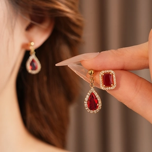 Close-up of luxury red teardrop earrings and square studs with gold setting and small diamonds