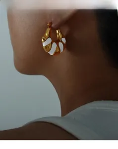 Dettaglio di orecchini smaltati bianchi su modella in finitura oro francese vintage