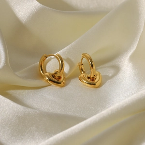 Vue détaillée de boucles d'oreilles créoles cœur dorées sur un tissu de soie blanche