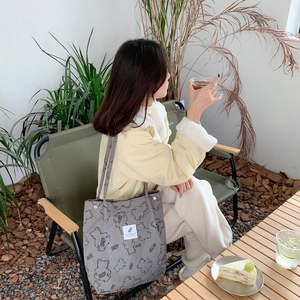 Detail of gray corduroy tote bag with bear print shown in a natural outdoor scene