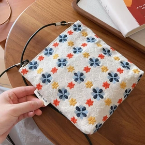 Gros plan de la broderie florale sur un sac à bandoulière en toile blanc cassé avec étiquette
