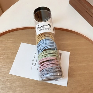 Detail of multi-color woven hair ties in a clear cylindrical bottle with handmade labels