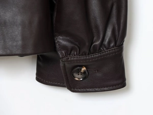 Detail of dark brown leather jacket cuff with button closure and fine stitching textures