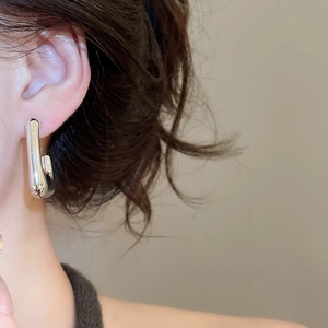 Close-up of a model wearing minimalist silver J-shaped earrings with a polished mirror finish