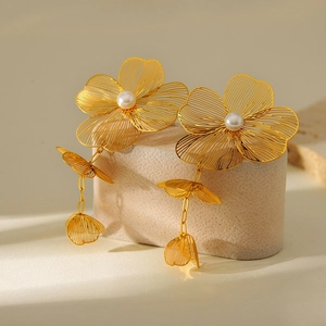 Detail of gold floral earrings with central pearl and elegant tassel on stone