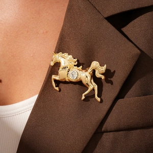 Detailed view of a golden horse brooch with sparkling crystal on a brown blazer