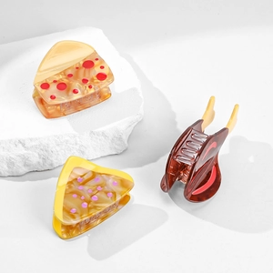 Three acetate fruit-inspired mini hair claws displayed on a textured stone over white