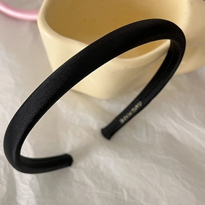 Close-up of black satin padded headband featuring a gold-stamped HAND MADE label inside