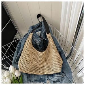 Detailed view of handmade woven straw tote bag with black trim and straps in a rustic basket