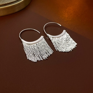 Detailed view of silver C-shaped metal tassel drop earrings on a warm vintage surface