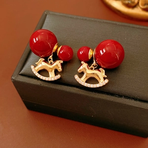 Detail of gold rocking horse earrings with red beads and zircon inlay on black gift box