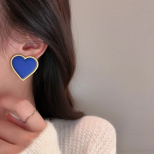 Close-up of elegant blue heart stud earrings with gold trim worn with a white sweater