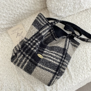 Detailed view of the fuzzy plaid tote bag featuring a metallic gold logo plaque and texture