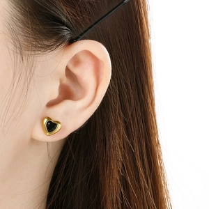Detail of a heart-shaped gold earring with black stone inlay worn on an ear