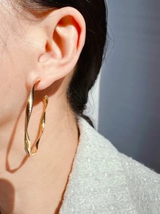 Close-up of golden oversized twisted hoop earrings with elegant wave texture on model