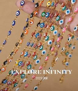Detail of hand holding multiple gold steel necklaces with colorful evil eye charms
