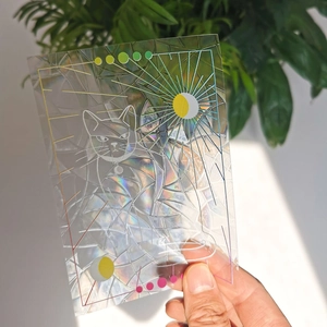 Rainbow prism suncatcher sticker with laser cat design held against green plants