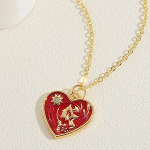 Macro shot of gold heart pendant with red enamel, dragon character, and tiny crystals