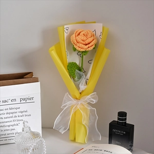 Detailed view of single handmade knitted orange rose wrapped in heart pattern yellow paper