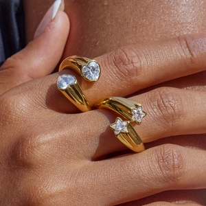 Detalle de anillos bañados en oro con circonitas de corazón y estrella en mano de modelo