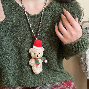 Detail of Christmas plush bear necklace with red scarf and hat on a green sweater