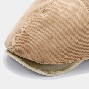 Detailed close-up of khaki corduroy fabric and metallic gold visor texture on the newsboy hat