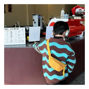 Detail of a bright yellow canvas waist bag for kids shown in a cozy cafe setting