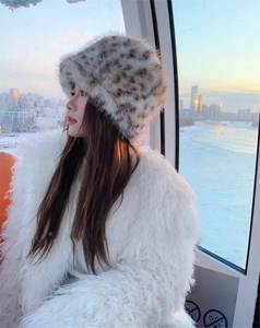 Close-up of leopard print faux fur bucket hat and white plush coat in snowy outdoor setting