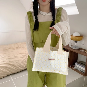 Detail of canvas lunch bag featuring white daisy patterns and cream woven handle strap