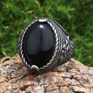 Detail of vintage eagle-patterned stainless steel ring with black oval gemstone on wood
