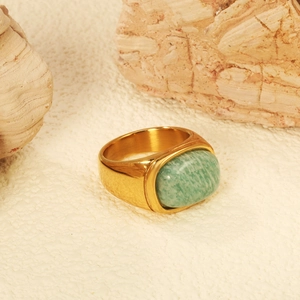 Gold ring with green oval gemstone on natural stone background in warm lighting