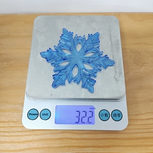 Blue acrylic hexagonal snowflake ornament weighing 32.2g on a scale for Christmas decor