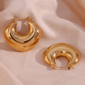 Macro view of gold-plated U-shaped chunky hoop earrings on elegant pink silk fabric