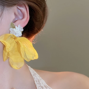 Close-up of yellow fabric flower earrings with pearl stamen on model in warm light