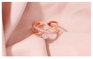 Detail shot of rose gold X-shaped ring with pave zircon stones on pink silk background
