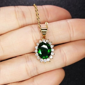 Macro shot of an oval emerald green gemstone pendant with white diamond halo in gold