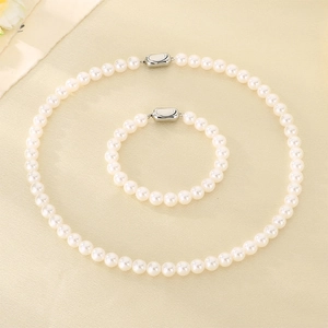 Vue détaillée de l'ensemble collier et bracelet en perles blanches sur tissu beige