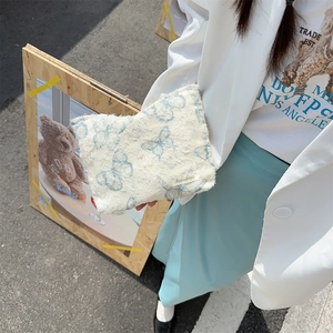 Detail of white lace butterfly makeup bag with fringe trim held by a model in a white blazer