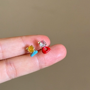 Close-up of asymmetric colorful zircon earrings with enamel held on fingers for scale.