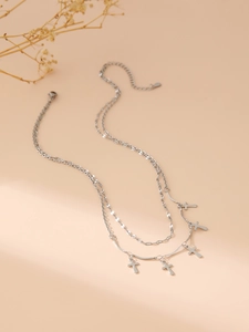 Detailed view of silver double-layered necklace with five small cross pendants on sand background