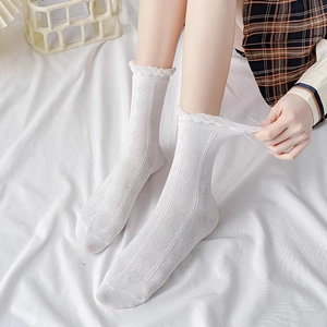 Chaussettes blanches en coton avec texture losange et bords volantés portées sur un lit blanc