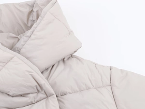 Detailed macro view of the stitching and fabric texture on a beige hooded puffer jacket