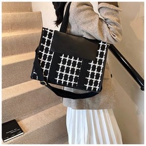 Detail view of the black and white checkered tote bag featuring a black flap and wide strap
