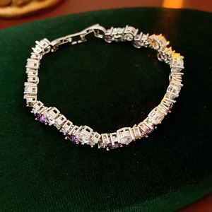 Close-up of silver-toned tennis bracelet with purple zircons on green velvet background