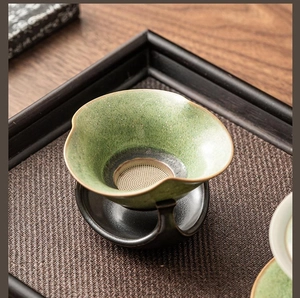 Close-up of a green glazed ceramic tea strainer with a black metal holder and base