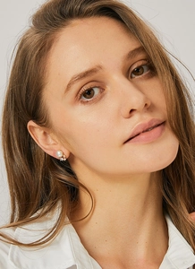 Close-up of pearl and zircon stud earrings worn by a model in elegant gold plating