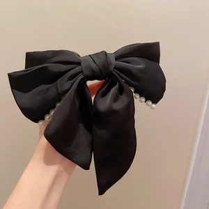 Détail d'une grande pince à cheveux nœud satin noir ornée d'une rangée de perles élégantes