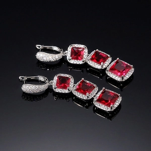 Macro detail of silver drop earrings featuring square red crystals and sparkling pavé accents