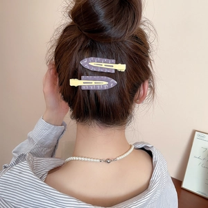 Detail of matte purple and yellow triangle hair clips worn with a pearl necklace