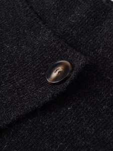 Close-up of black knitted fabric with an amber-textured resin button on asymmetric midi skirt
